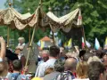 Procesja 19 czerwca. Ludzie obserwują uroczystość pod ozdobnym baldachimem, niektórzy filmują telefonami.