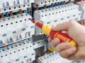 Dłoń trzymająca śrubokręt przy skrzynce z bezpiecznikami. To praca na **dzień elektryka**, gdzie precyzja jest kluczowa.