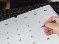 Dłoń z długopisem zaznacza datę 11 maja na kalendarzu. Obok leży klawiatura.