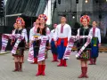 Grupa młodych ludzi w tradycyjnych strojach ludowych, świętująca imieniny Lecha. Dziewczęta w kolorowych wiankach i haftowanych sukniach, chłopcy w białych koszulach i niebieskich spodniach.