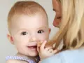 Uśmiechnięte dziecko trzymane przez mamę, bawiące się jej włosami.