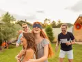 Radosna ciuciubabka zabawa w ogrodzie. Dziewczyna z zawiązanymi oczami śmieje się, podczas gdy jej przyjaciele ją prowadzą.