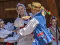 Młoda para w strojach ludowych tańczy z uśmiechem. Chłopak w słomkowym kapeluszu, dziewczyna w kwiecistej chustce. Licho co to za piękny widok!