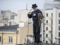 Kominiarz w cylindrze i czarnym stroju przygotowuje się do pracy, trzymając linę. To jego dzień, dzień kominiarza.