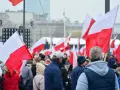 Tłum ludzi z polskimi flagami. W tle scena i budynki. Może to być związane z jakimś wydarzeniem narodowym, ale nie ma informacji, jakie święto jest 11 października.