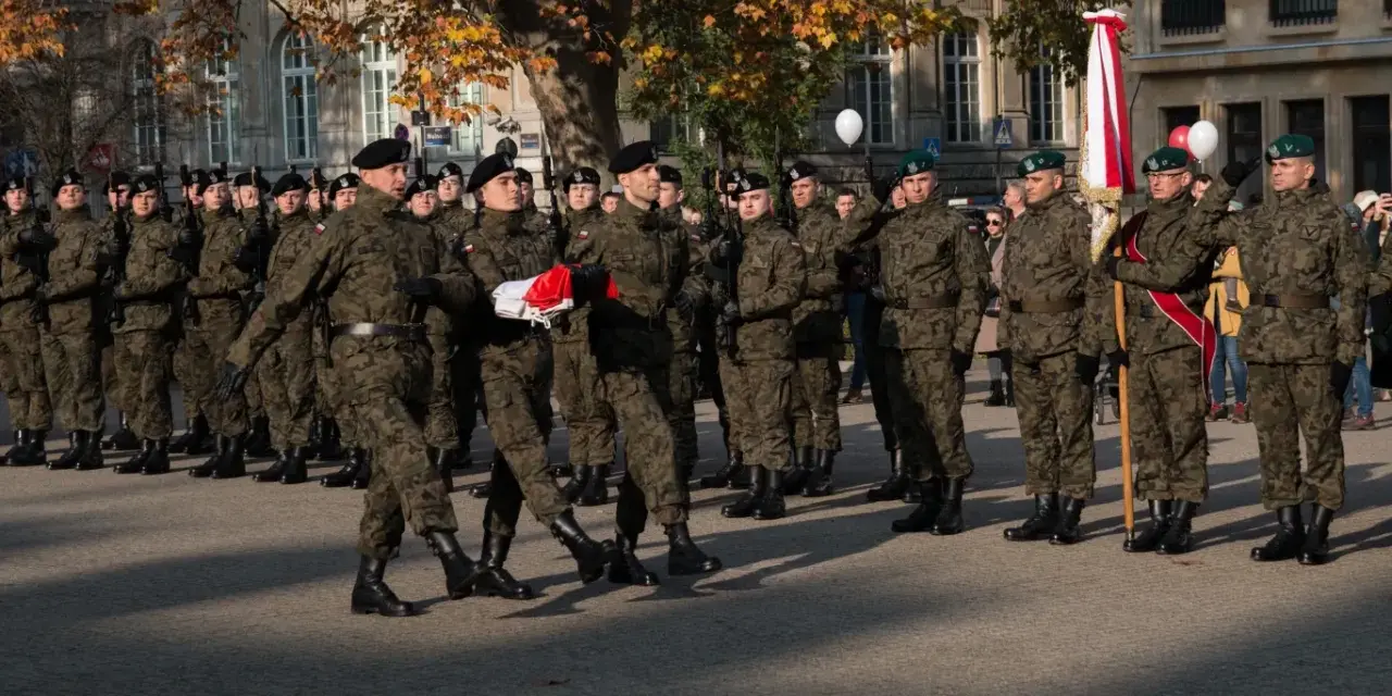 Żołnierze w mundurach stoją w szeregu. 28 listopada święto upamiętnia ważne wydarzenia. W tle drzewa i budynki.