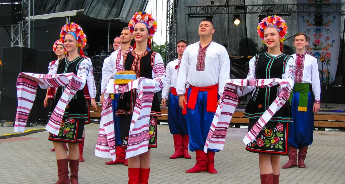 Grupa młodych ludzi w tradycyjnych strojach ludowych, świętująca imieniny Lecha. Dziewczęta w kolorowych wiankach i haftowanych sukniach, chłopcy w białych koszulach i niebieskich spodniach.