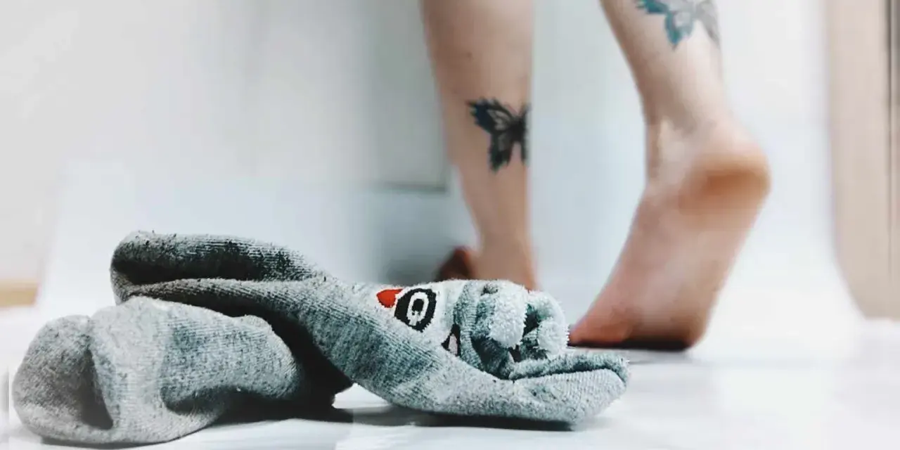 21 października nietypowe święta. Skarpetka z motywem rekina leży obok stóp z tatuażami motyli.