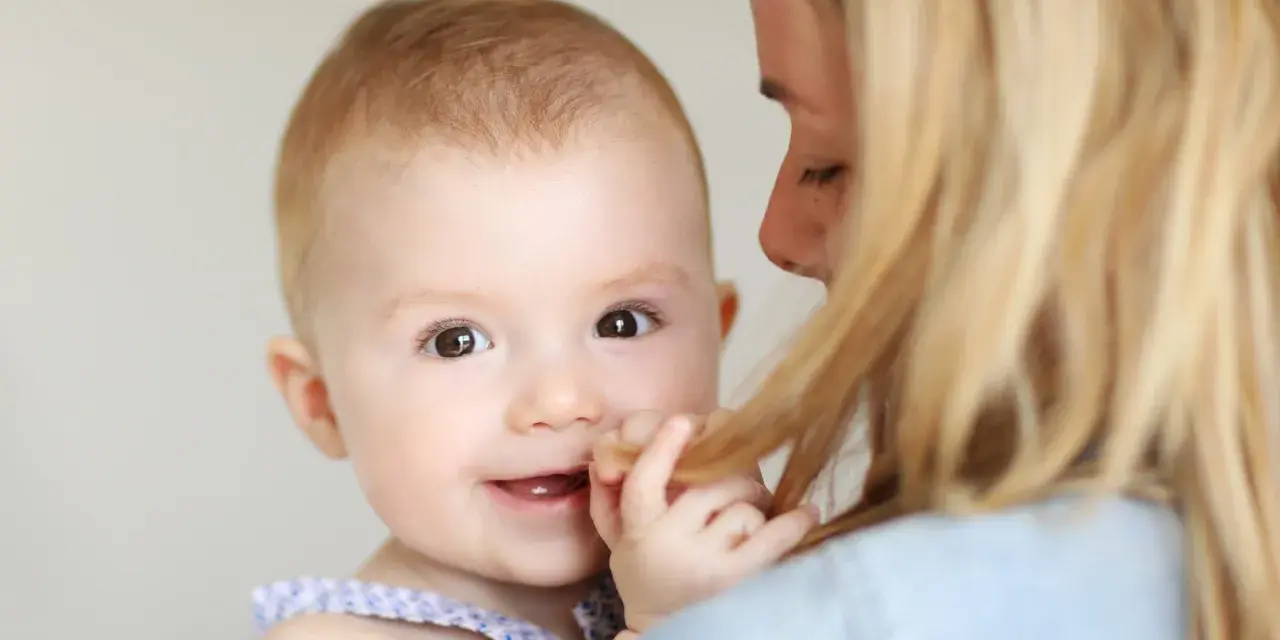 Uśmiechnięte dziecko trzymane przez mamę, bawiące się jej włosami.