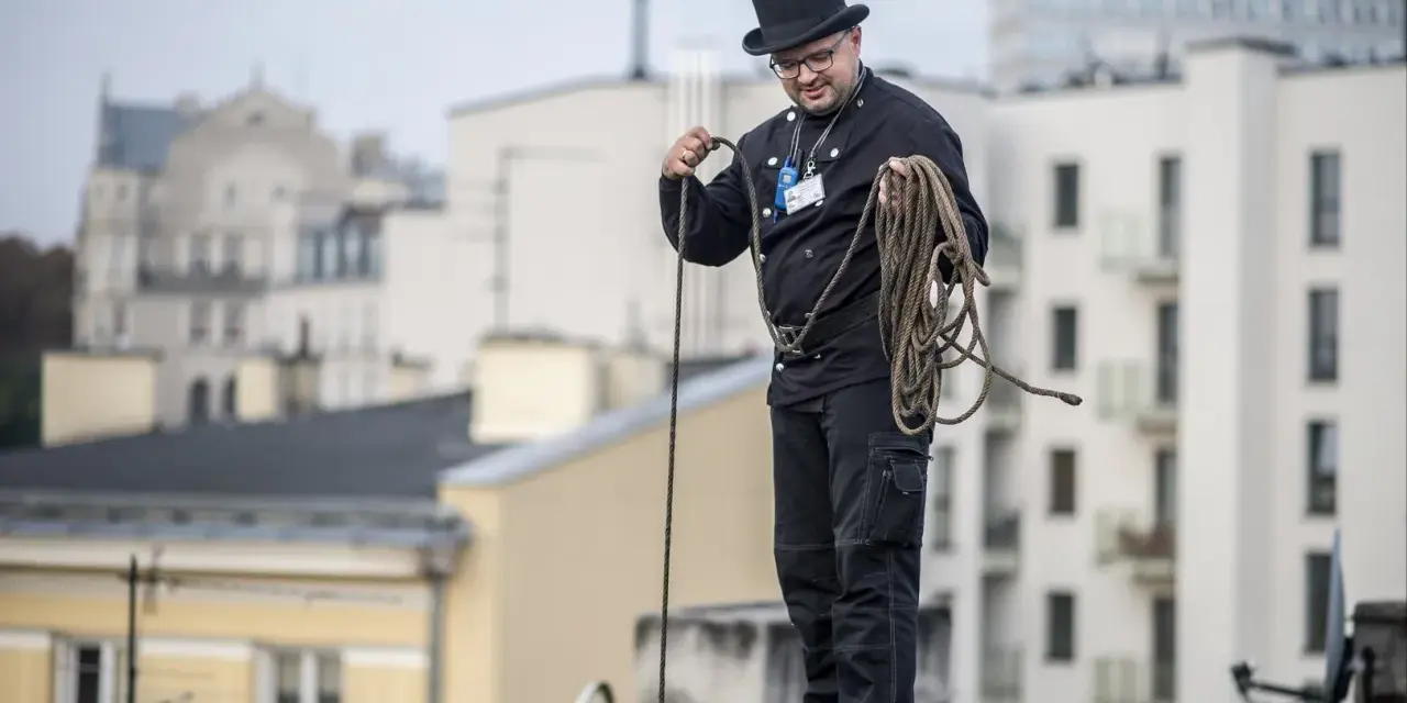 Kominiarz w cylindrze i czarnym stroju przygotowuje się do pracy, trzymając linę. To jego dzień, dzień kominiarza.