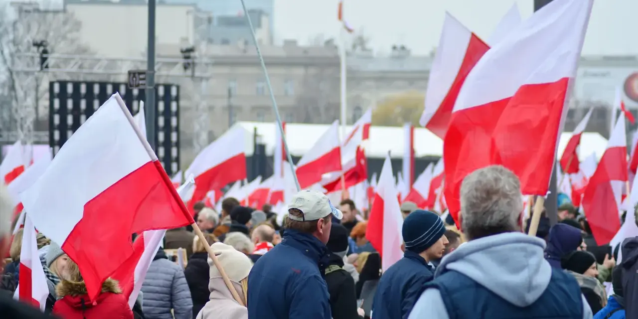 Tłum ludzi z polskimi flagami. W tle scena i budynki. Może to być związane z jakimś wydarzeniem narodowym, ale nie ma informacji, jakie święto jest 11 października.