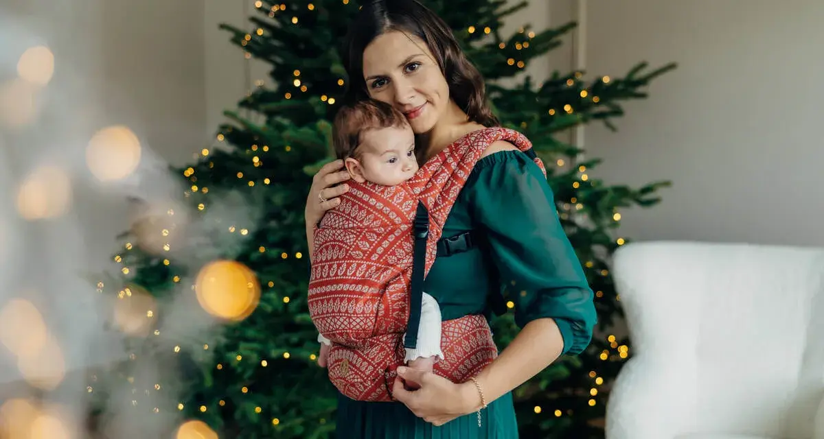 26 października nietypowe święta. Mama z dzieckiem w chuście przy choince, otuleni ciepłem i świąteczną atmosferą.