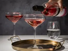 Różowe wino nalewane do kieliszków. Zastanawiasz się, jakie kieliszki do jakiego wina? Tutaj widzimy kieliszki typu coupe, idealne do szampana i lekkich win musujących.