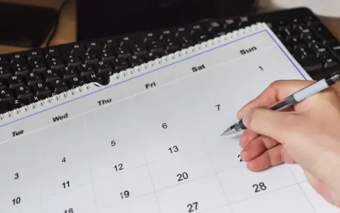 Dłoń z długopisem zaznacza datę 11 maja na kalendarzu. Obok leży klawiatura.