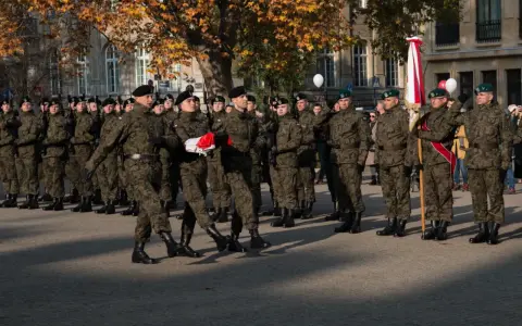 Żołnierze w mundurach stoją w szeregu. 28 listopada święto upamiętnia ważne wydarzenia. W tle drzewa i budynki.
