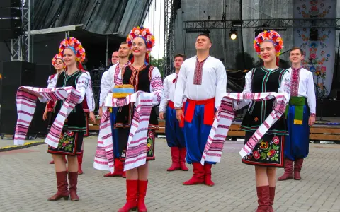 Grupa młodych ludzi w tradycyjnych strojach ludowych, świętująca imieniny Lecha. Dziewczęta w kolorowych wiankach i haftowanych sukniach, chłopcy w białych koszulach i niebieskich spodniach.