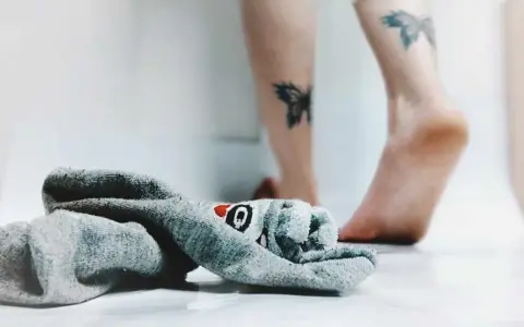 21 października nietypowe święta. Skarpetka z motywem rekina leży obok stóp z tatuażami motyli.