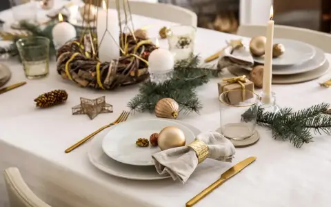 Elegancka dekoracja stołu na Boże Narodzenie: złote ozdoby, świece, gałązki choinki i orzechy tworzą magiczny nastrój.