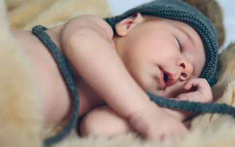 Słodki maluszek w czapce z pomponem śpi na miękkim futerku. Może to jego pierwsze imieniny Tymona?