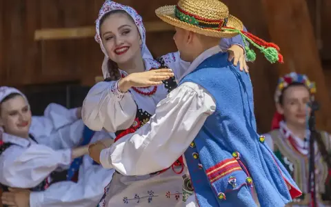 Młoda para w strojach ludowych tańczy z uśmiechem. Chłopak w słomkowym kapeluszu, dziewczyna w kwiecistej chustce. Licho co to za piękny widok!