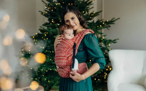 26 października nietypowe święta. Mama z dzieckiem w chuście przy choince, otuleni ciepłem i świąteczną atmosferą.