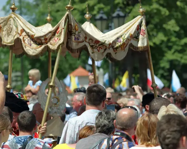 Procesja 19 czerwca. Ludzie obserwują uroczystość pod ozdobnym baldachimem, niektórzy filmują telefonami.