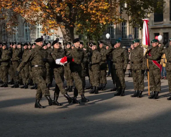 Żołnierze w mundurach stoją w szeregu. 28 listopada święto upamiętnia ważne wydarzenia. W tle drzewa i budynki.