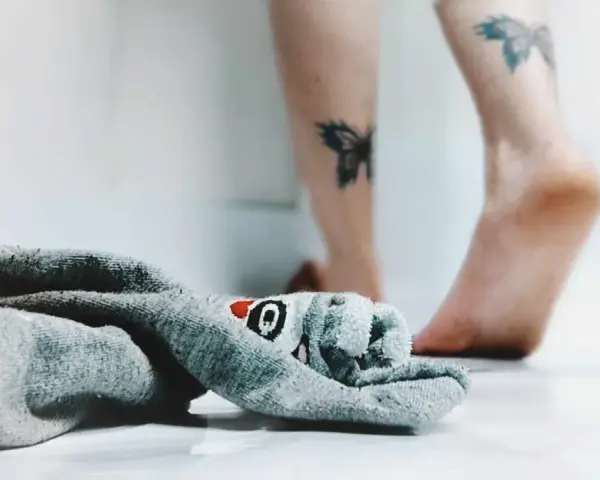 21 października nietypowe święta. Skarpetka z motywem rekina leży obok stóp z tatuażami motyli.