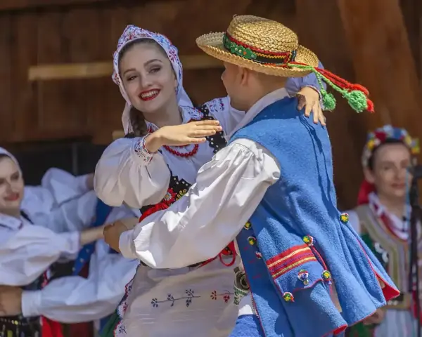 Młoda para w strojach ludowych tańczy z uśmiechem. Chłopak w słomkowym kapeluszu, dziewczyna w kwiecistej chustce. Licho co to za piękny widok!