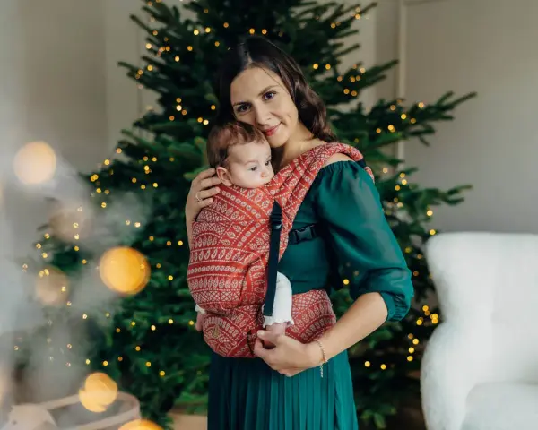 26 października nietypowe święta. Mama z dzieckiem w chuście przy choince, otuleni ciepłem i świąteczną atmosferą.