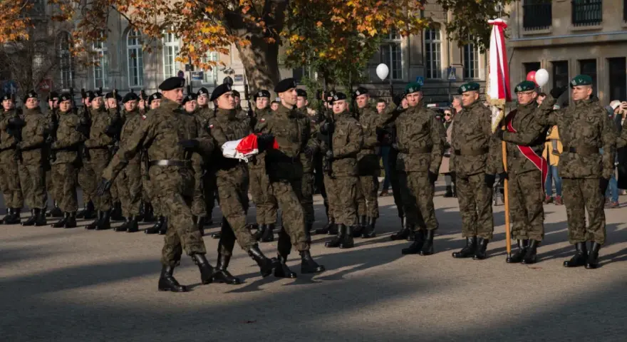 Żołnierze w mundurach stoją w szeregu. 28 listopada święto upamiętnia ważne wydarzenia. W tle drzewa i budynki.