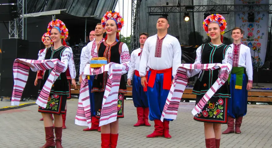 Grupa młodych ludzi w tradycyjnych strojach ludowych, świętująca imieniny Lecha. Dziewczęta w kolorowych wiankach i haftowanych sukniach, chłopcy w białych koszulach i niebieskich spodniach.