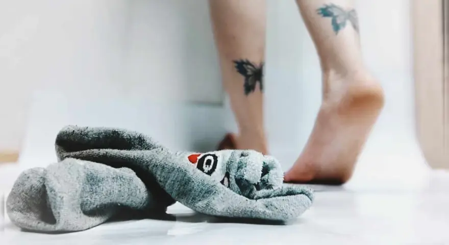 21 października nietypowe święta. Skarpetka z motywem rekina leży obok stóp z tatuażami motyli.