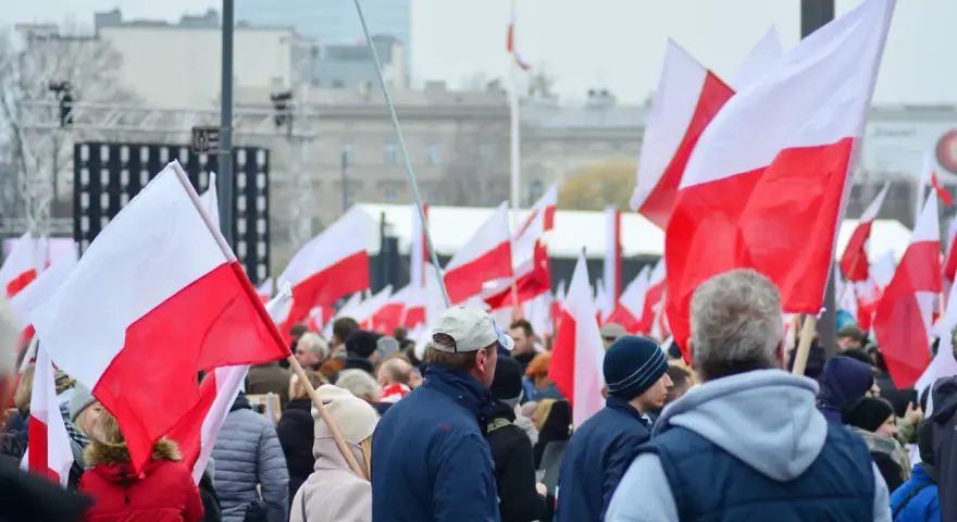 Tłum ludzi z polskimi flagami. W tle scena i budynki. Może to być związane z jakimś wydarzeniem narodowym, ale nie ma informacji, jakie święto jest 11 października.
