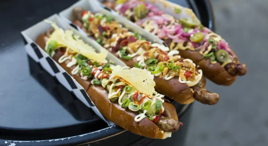 Trzy apetyczne hot dogi z różnymi dodatkami, idealne na 15 lipca nietypowe święta.