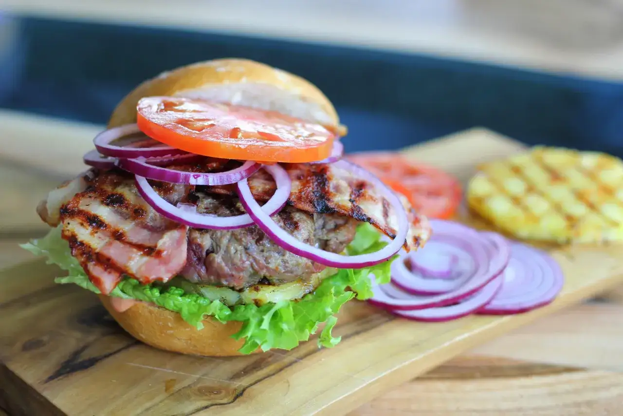 Pyszny burger z bekonem, sałatą, pomidorem i czerwoną cebulą. Idealny na dzień burgera!