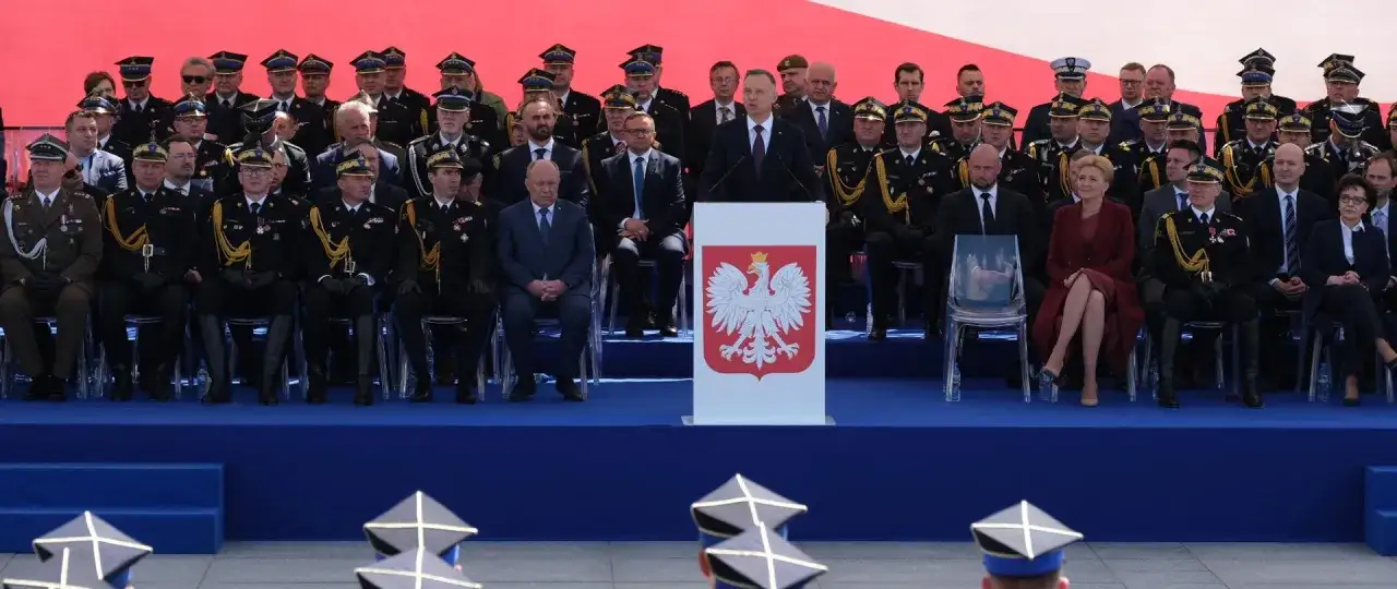 Uroczystość z okazji dnia strażaka. Prezydent Duda przemawia, a obok siedzą strażacy w galowych mundurach i zaproszeni goście.