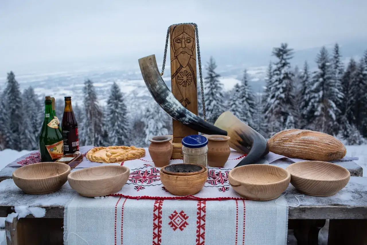 St&oacute;ł z tradycyjnymi potrawami i napojami, gotowy na szczodre gody. Wśr&oacute;d nich rogi do picia, chleb, ciasto i drewniane misy.