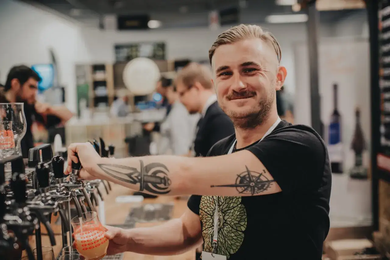 Uśmiechnięty barman z tatuażami nalewa piwo. Idealny dzień piwa, pełen radości i pysznego trunku.