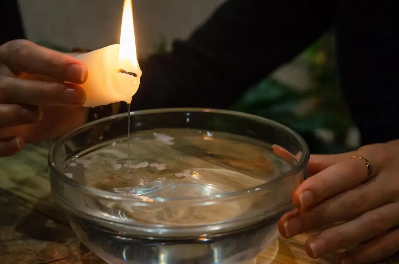 Kropla woskowa z płonącej świecy spada do miski z wodą, tworząc kształty zapowiadające andrzejkowe wr&oacute;żby.