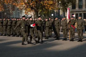 Żołnierze w mundurach stoją w szeregu. 28 listopada święto upamiętnia ważne wydarzenia. W tle drzewa i budynki.