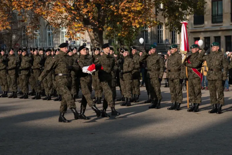 Żołnierze w mundurach stoją w szeregu. 28 listopada święto upamiętnia ważne wydarzenia. W tle drzewa i budynki.